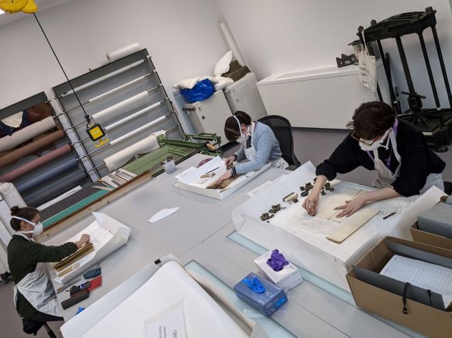 Three people sitting around a work bench cleaning archive items.