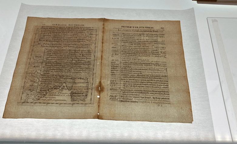 Cream coloured paper bifolio on light table shows brighter areas where paper is missing.