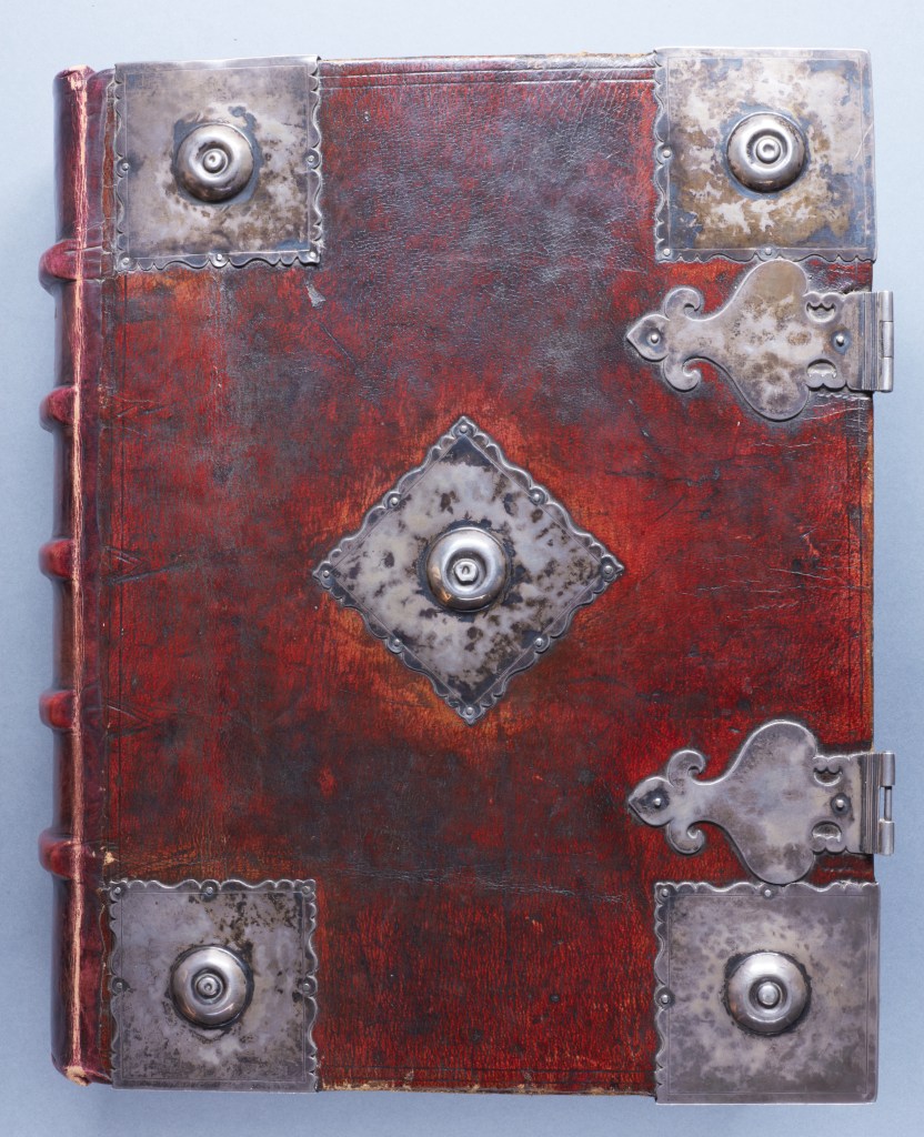 A book bound in red leather with prominent silver bosses in the corners and centre.