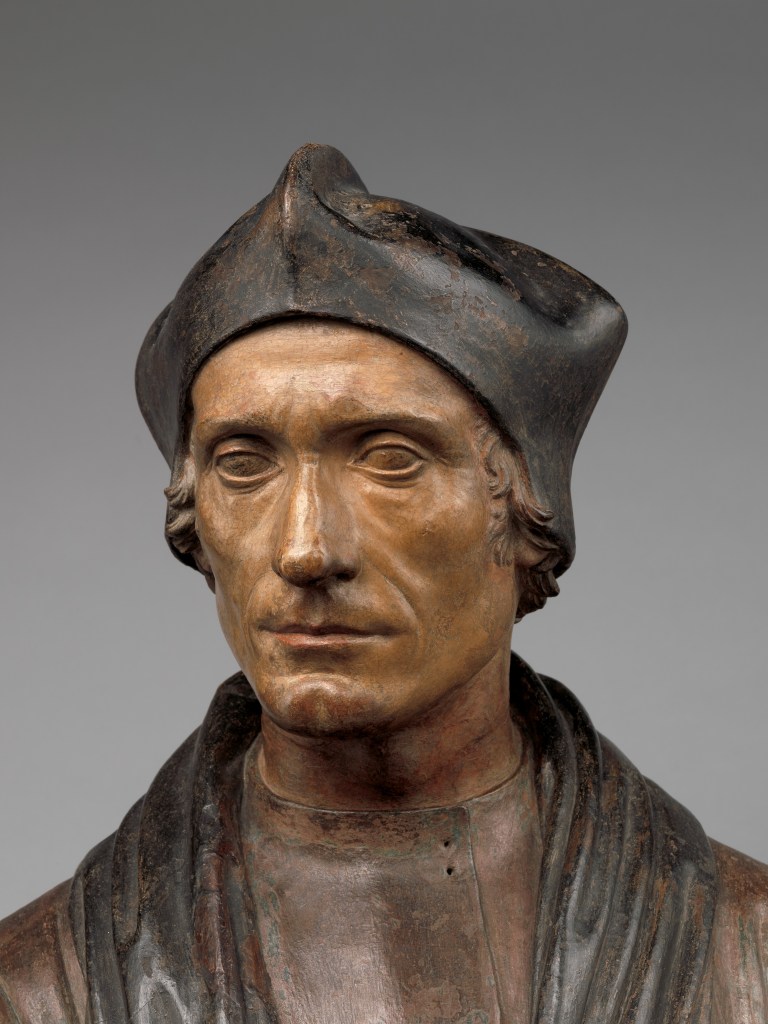 16th Century sculpture of a man in clerical robes and black cap.
